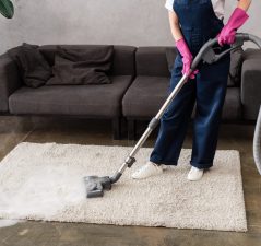 Cropped view of cleaner in overalls and rubber gloves using vacuum cleaner with hot steam on carpet