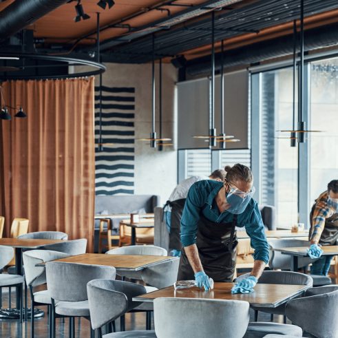 Wait staff in protective workwear cleaning tables in restaurant